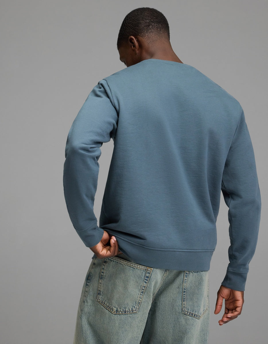 A person wearing the Cozy Earth Men’s Dylan Crewneck and light blue jeans stands with their back to the camera against a plain gray background.