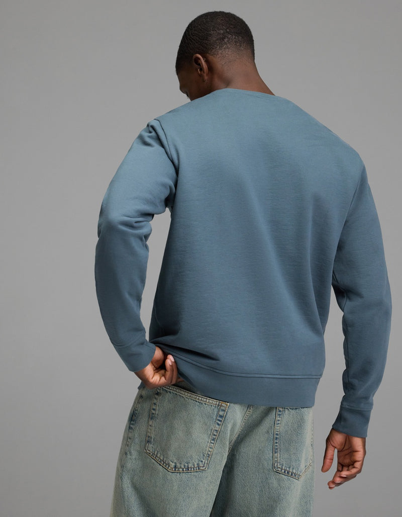 A person wearing the Cozy Earth Men’s Dylan Crewneck and light blue jeans stands with their back to the camera against a plain gray background.