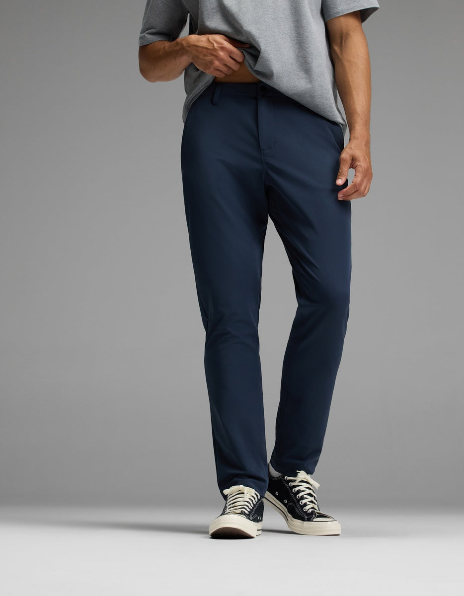 A person wearing Cozy Earth’s Men’s Everywhere Pant in navy blue, paired with a grey t-shirt and black low-top sneakers, stands against a plain grey background. Their head is not visible in the image.|Color:Eclipse