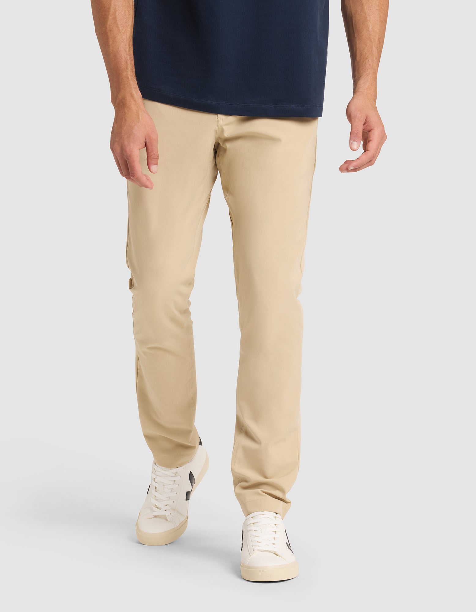 A model wears Cozy Earth's Men's Everywhere Pant in beige, paired with a navy shirt and white sneakers with black accents, standing against a plain light gray background. The image is cropped from the shoulders down. |Color:Khaki