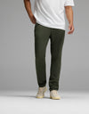 A person wearing Cozy Earth’s Men’s Everywhere Pant in olive green is pictured standing against a plain gray background. The image is cropped at the shoulders, focusing on the lower torso and legs.|Color:Olive