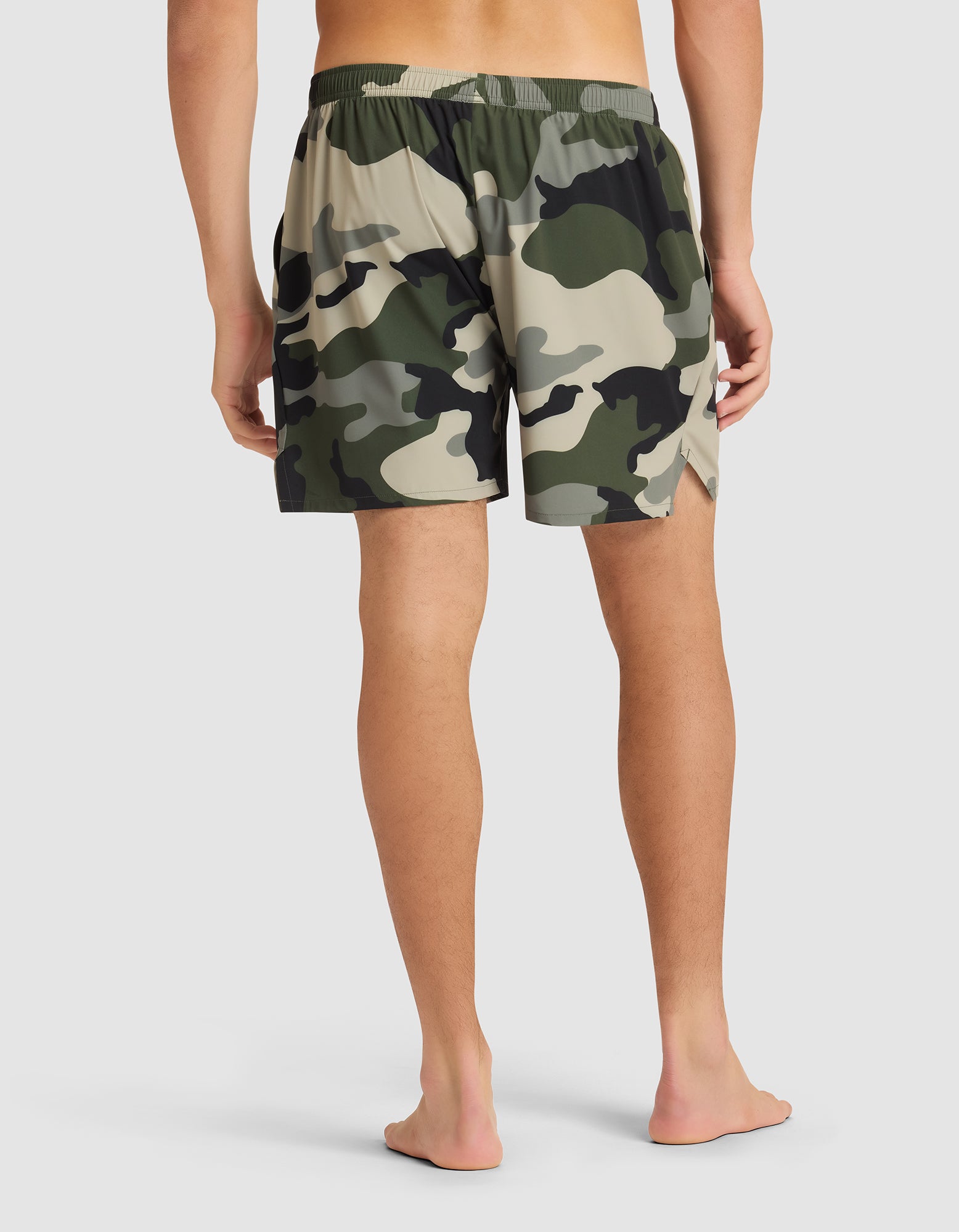 A person stands barefoot, facing away, wearing Cozy Earth Men's Day & Night Shorts 5" with an elastic waistband and a green, beige, and black camouflage pattern against a plain light background. |Color:Cypress Camo