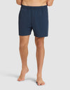 A person stands barefoot against a plain light background, wearing Cozy Earth Men's Day & Night Shorts 5" in dark blue with an elastic waistband. The upper body and head are not visible. |Color:Eclipse