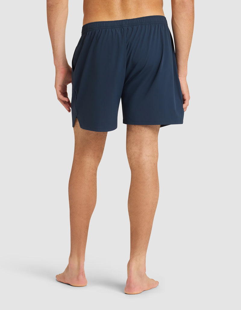 A person stands barefoot facing away, wearing Cozy Earth Men's Day & Night Shorts 5" in navy with an elastic waistband and side slits, set against a plain light background.
