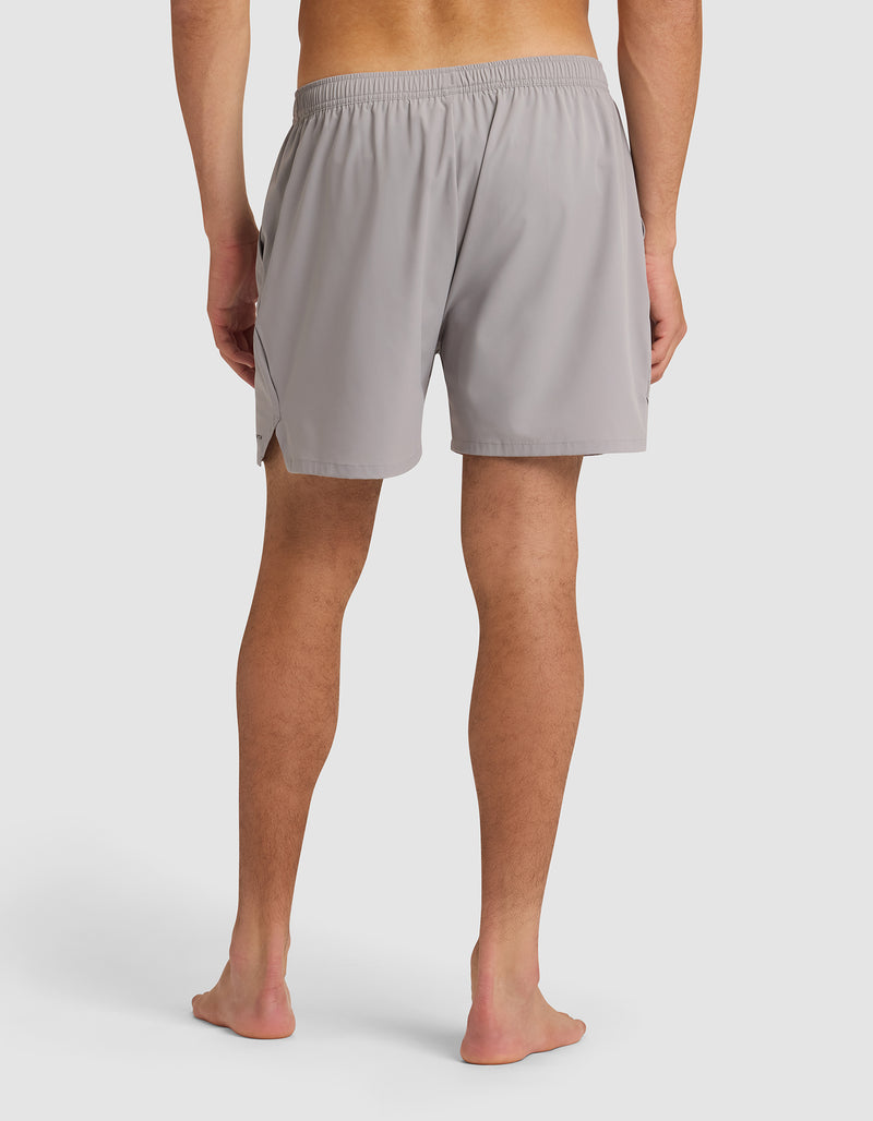 A man stands barefoot, facing away from the camera, wearing Cozy Earth Men's Day & Night Shorts 5" in light gray with an elastic waistband, set against a plain white background.