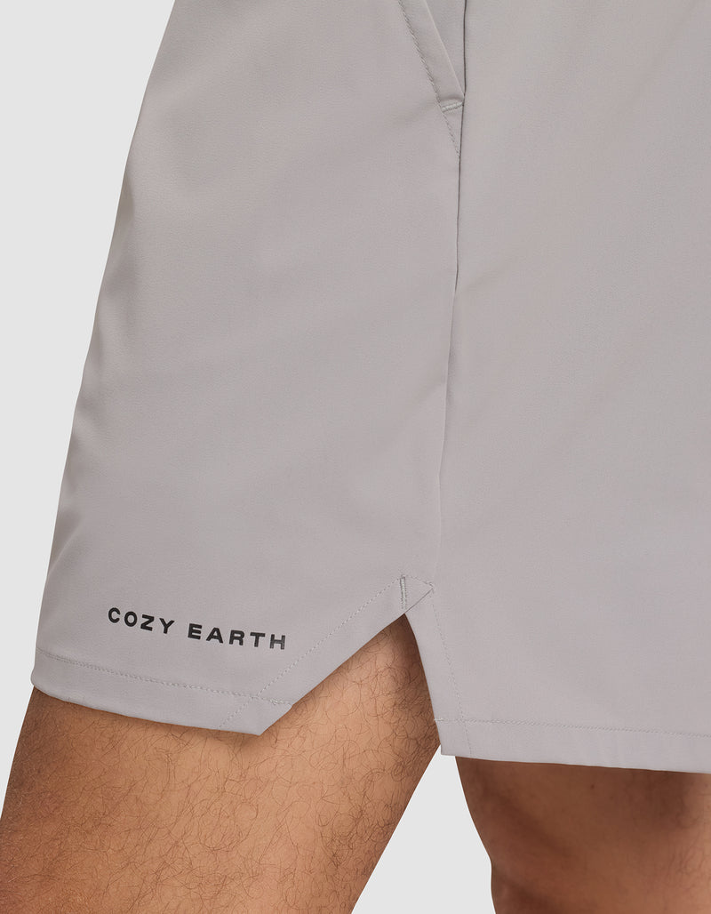 A close-up of a person wearing Cozy Earth Men's Day & Night Shorts 5" in light gray, featuring the brand name near the left hem, a small side slit, and a visible pocket seam.