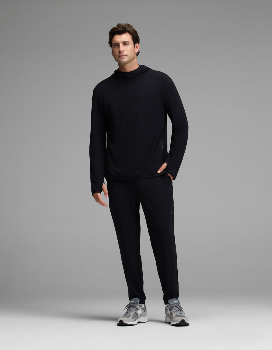 A man stands facing forward wearing Cozy Earth’s Men’s Recovery Jogger in black, paired with a black long-sleeve shirt and gray sneakers against a plain light gray background.