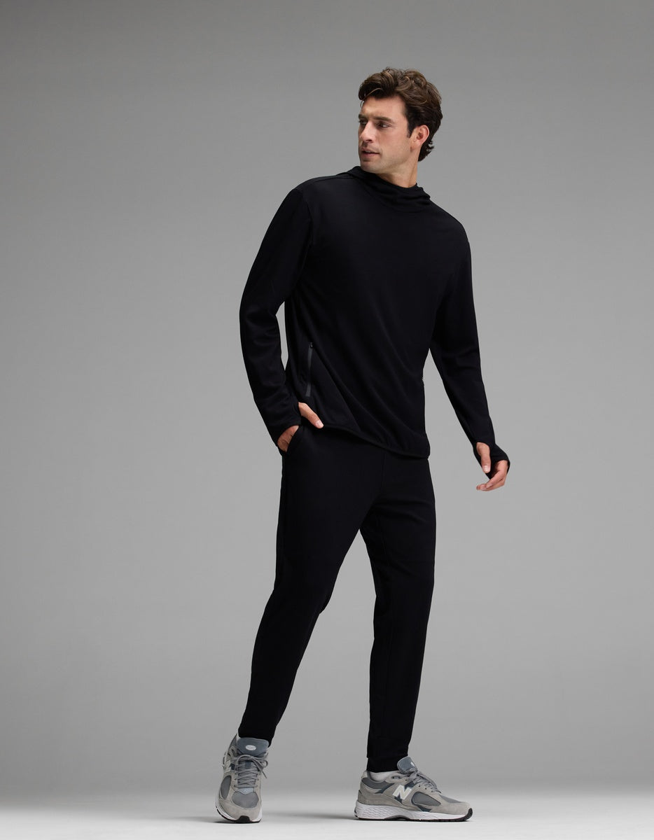 A man is seen wearing the Cozy Earth Men’s Recovery Hoodie & Jogger Set in black, paired with gray sneakers, as he stands against a plain gray background and looks to his left.