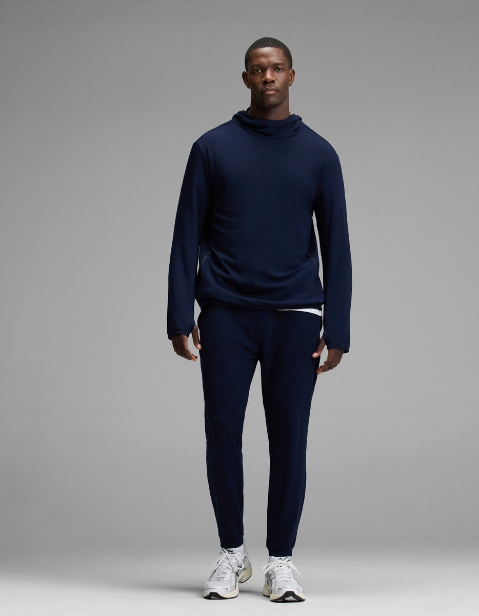 A man stands facing forward, wearing the Cozy Earth Men’s Recovery Jogger set in navy blue with white sneakers, against a plain gray background.