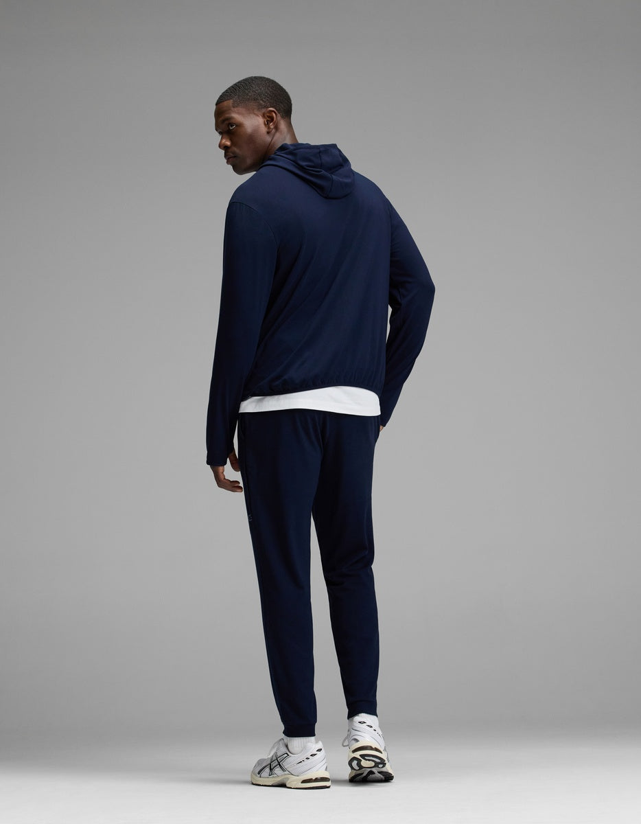 A man wearing Cozy Earth’s Men’s Recovery Jogger in navy, paired with a white T-shirt and white sneakers, stands facing away and glances over his left shoulder against a plain gray background.|Color:Navy