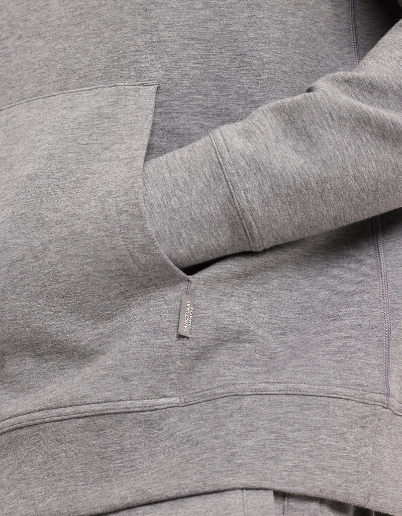 A person in a gray Men's StretchTech Hoodie by Cozy Earth has their hand in the front pocket, highlighting the fabric's texture and details.
