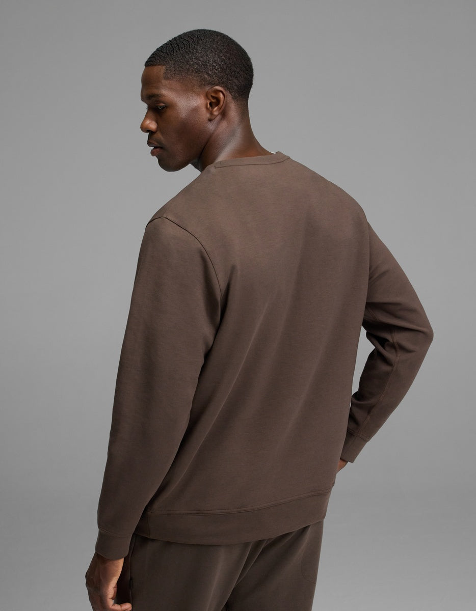 A man stands facing away, wearing the Cozy Earth Men’s StretchTech Crewneck and matching pants against a plain gray background.|Color:Cacao