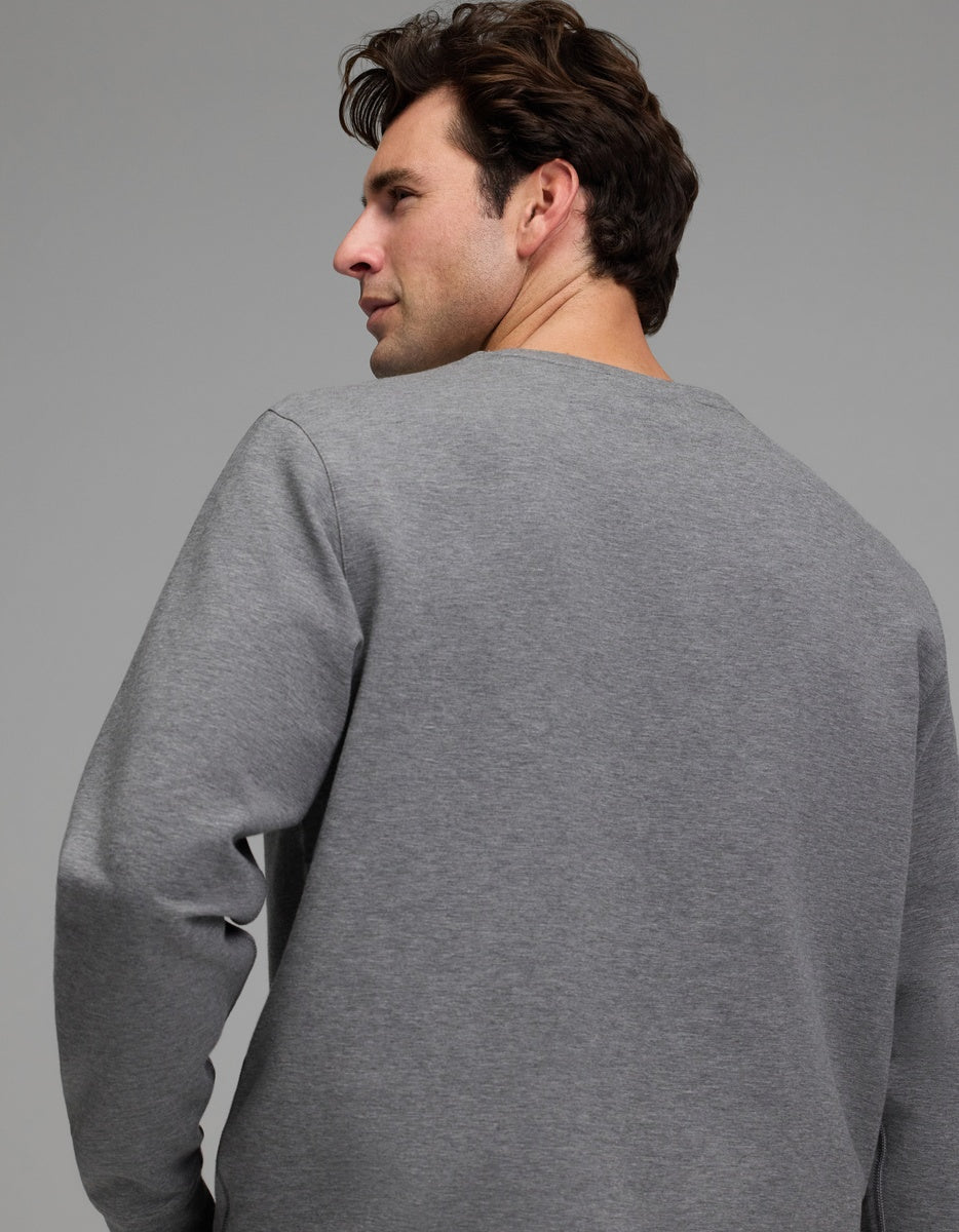 A man with brown hair wears the Cozy Earth Men’s StretchTech Crewneck and looks over his shoulder against a neutral gray background.