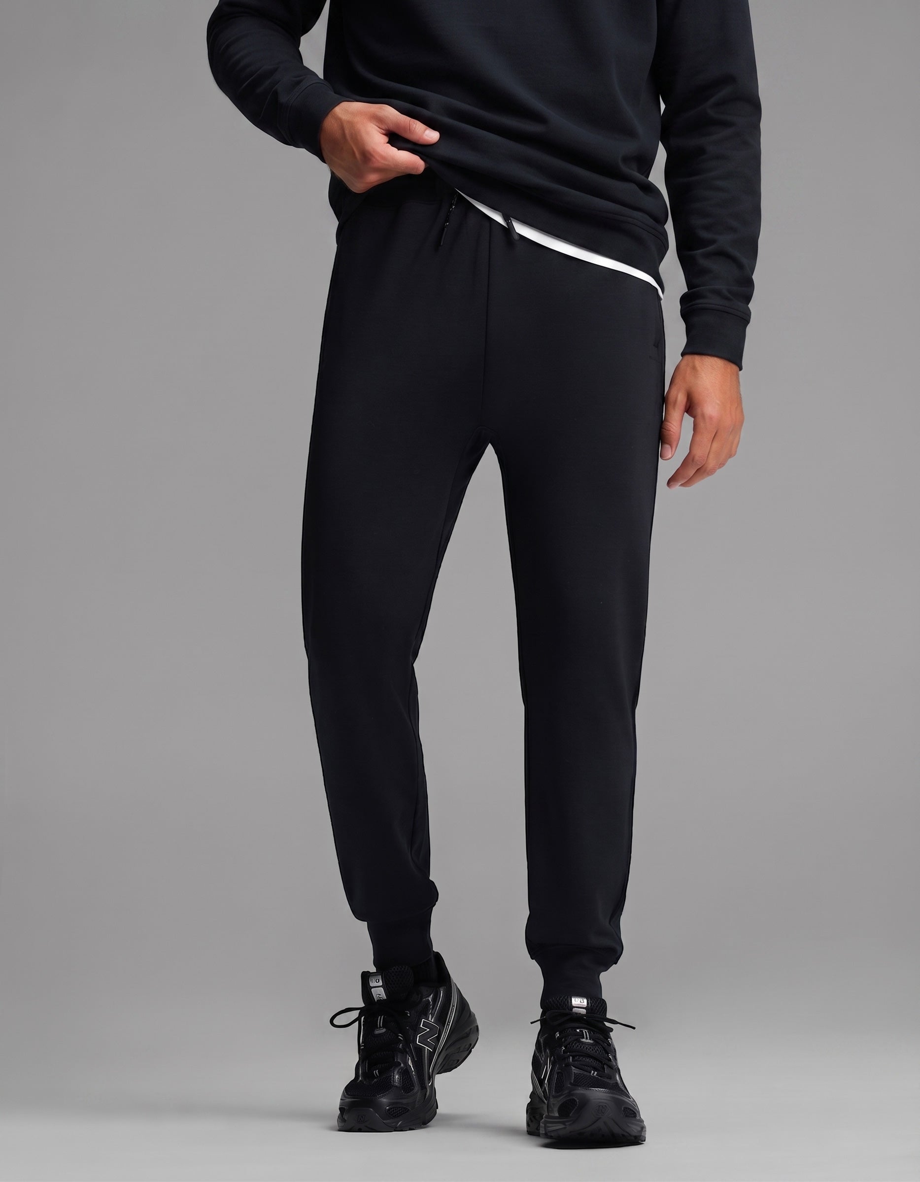 A person is shown standing against a plain gray background wearing the Men's Versa Crewneck & Jogger Set in black by Cozy Earth. Their face is not visible in the image.