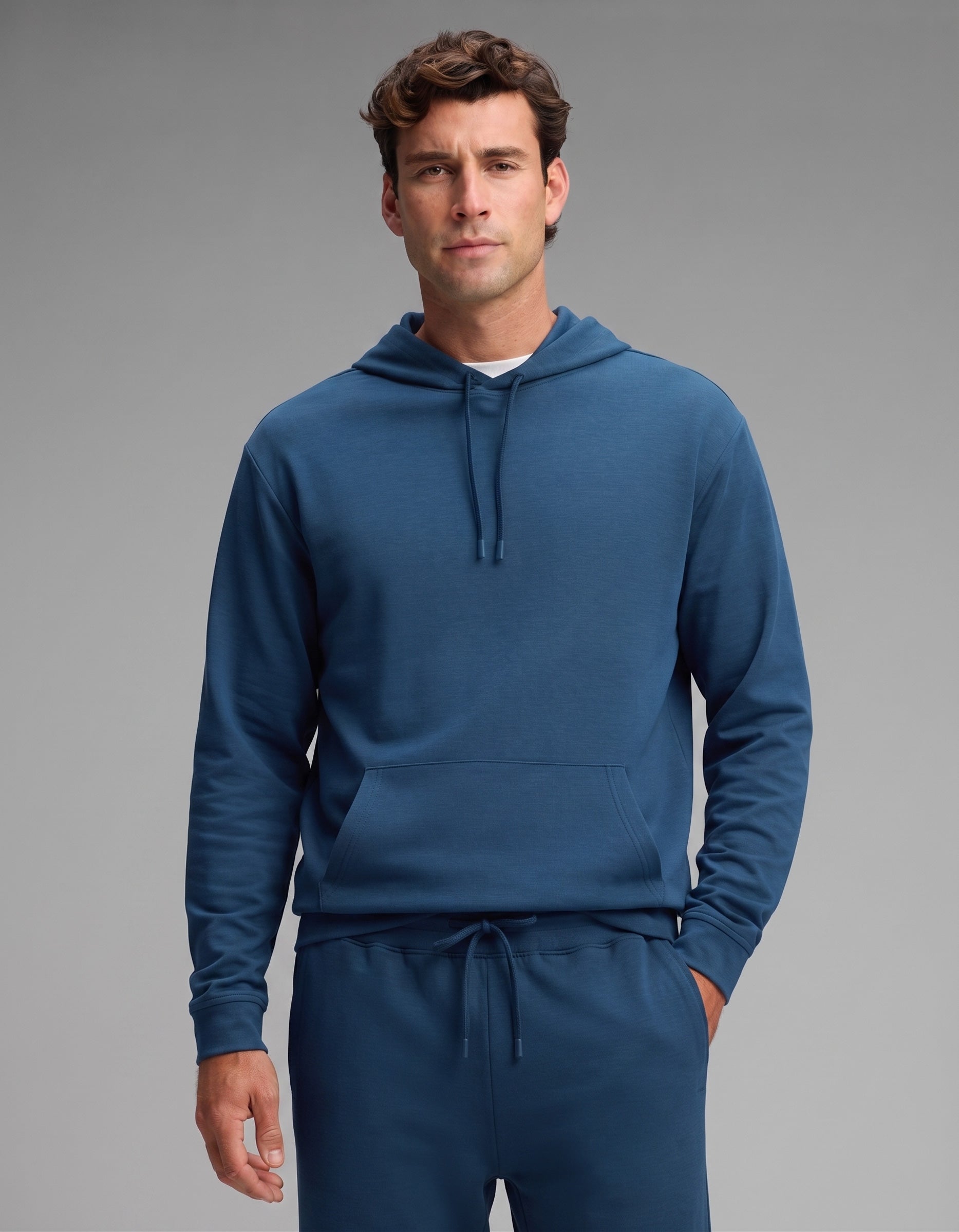 A man stands facing forward against a plain gray background, wearing the Cozy Earth Men's Versa Hoodie & Jogger Set in blue.