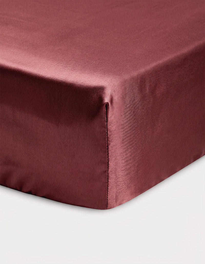 Close-up of a corner of a bed showcasing the Cozy Earth Bamboo Fitted Sheet in maroon, neatly covering the mattress against a white background.