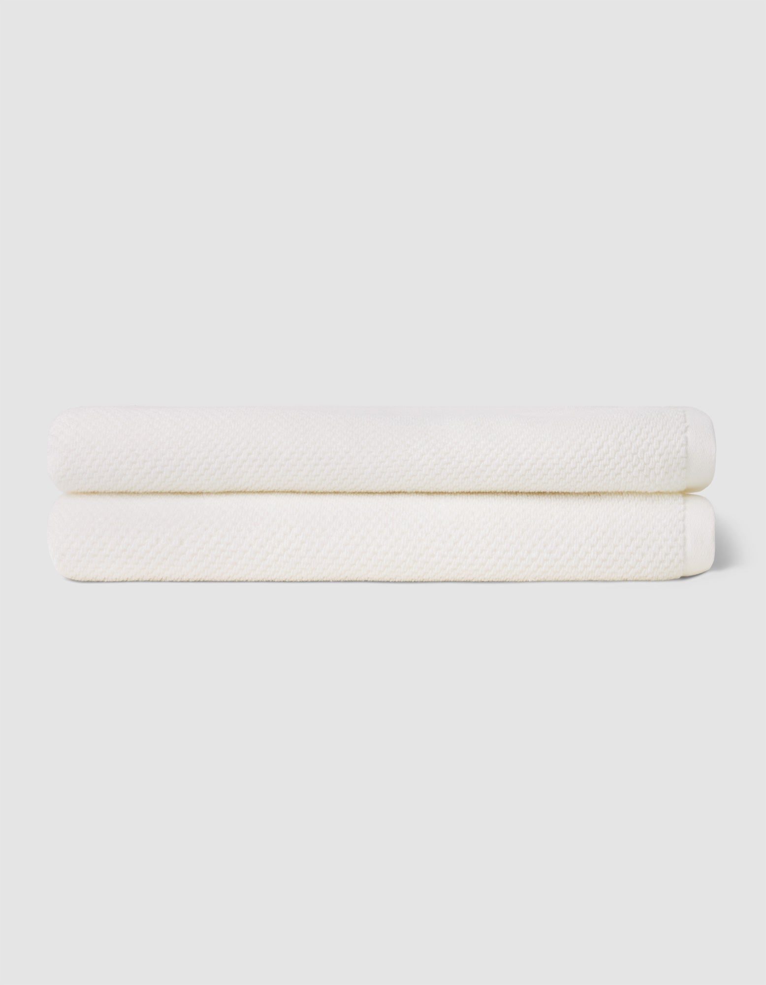 Two neatly folded Cozy Earth Nantucket Bath Sheets are stacked atop each other against a plain, light-colored background.|Color:White