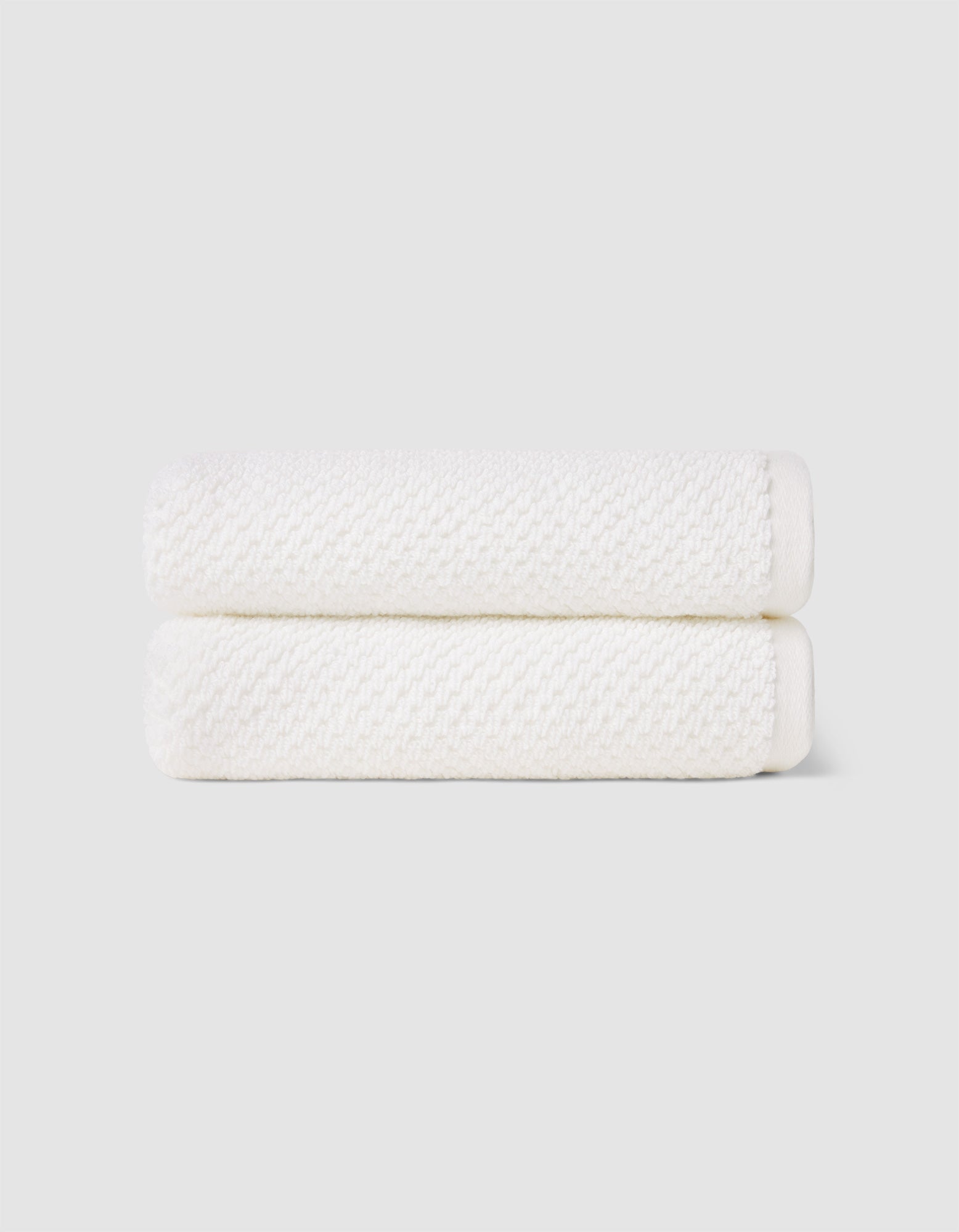Two Nantucket Hand Towels by Cozy Earth, neatly folded and stacked, are displayed against a plain light gray background.|Color:White