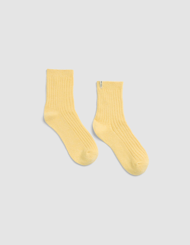 The Plush Lounge Quarter Socks by Cozy Earth in light yellow, featuring a ribbed crew design, is displayed laid flat on a light gray background.