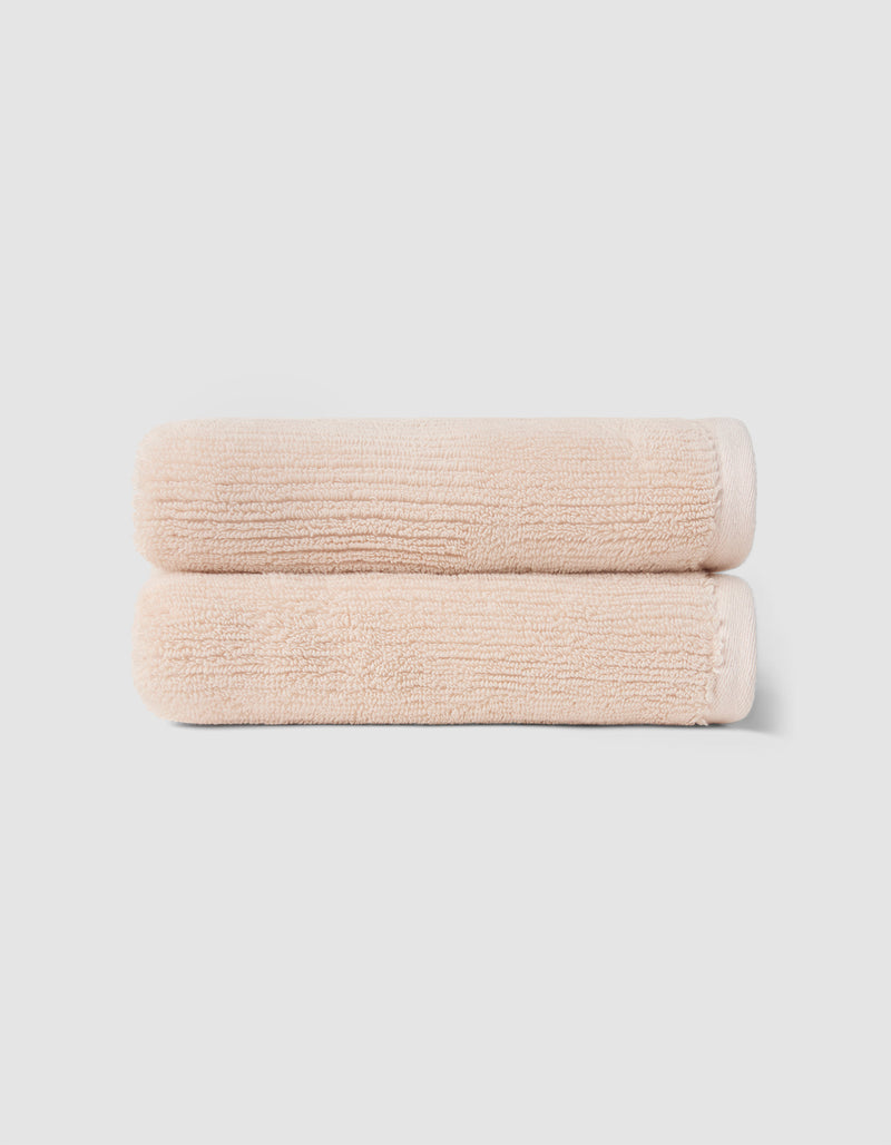 The Cozy Earth Complete Ribbed Terry Bath Bundle features two neatly folded, light beige towels stacked atop each other against a plain, light gray background.