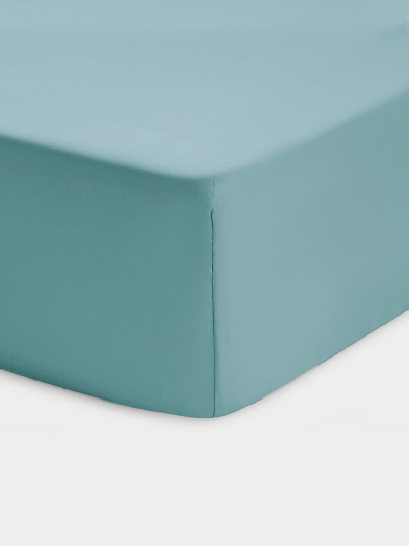 Close-up of a corner of a bed showcasing the Cozy Earth Bamboo Fitted Sheet in light blue, neatly covering the mattress against a white background.