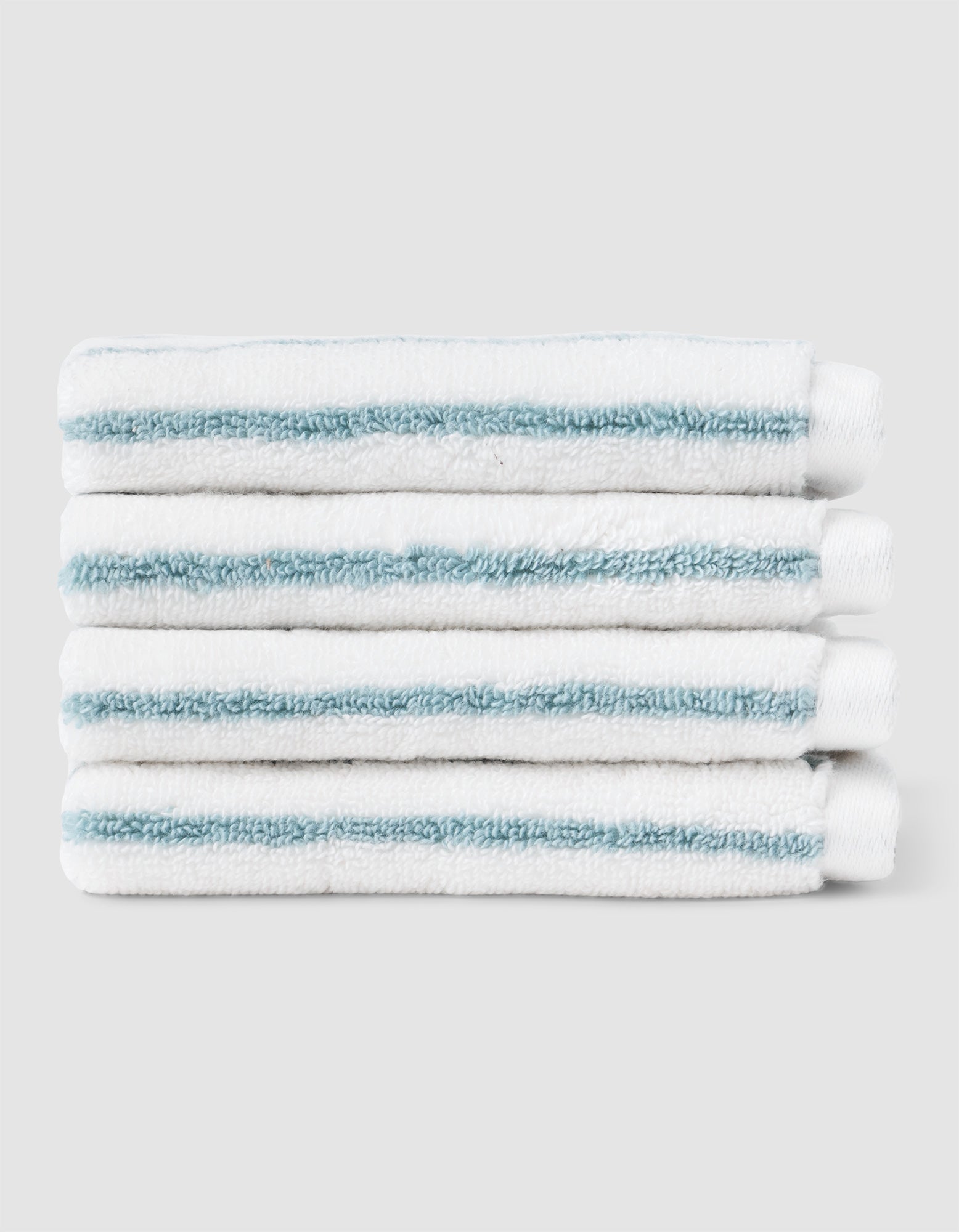 Five Striped Luxe Washcloths by Cozy Earth, white with light blue stripes, are neatly stacked against a plain light gray background. |Color:Brook Stripe