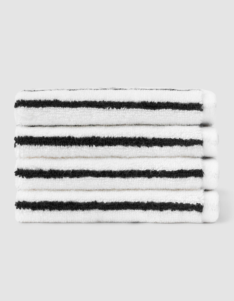 A stack of four neatly folded Cozy Earth Striped Luxe Washcloths in white with evenly spaced black stripes, set against a plain light gray background.
