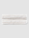 Two Striped Luxe Bath Sheets by Cozy Earth, featuring white fabric with thin, evenly spaced tan stripes, are neatly folded and stacked against a plain light gray background.  |Color:Sand Stripe