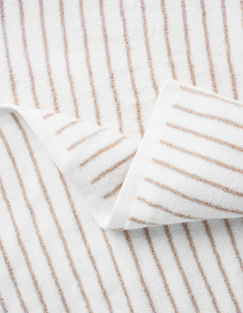 A close-up of Cozy Earth’s Striped Luxe Bath Sheets, featuring thin, evenly spaced brown stripes on a white background and folded to highlight their soft texture and elegant pattern.
