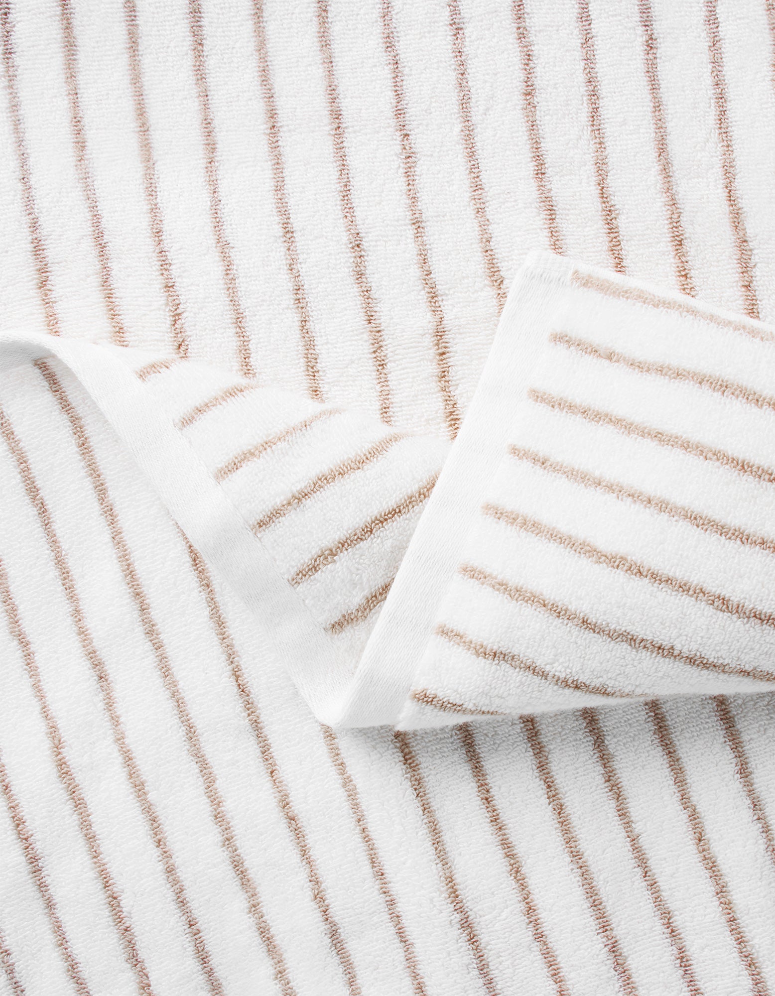 A close-up of Cozy Earth's Striped Luxe Washcloths shows evenly spaced brown stripes on white fabric, with one corner folded to display the signature striped pattern on both sides. 