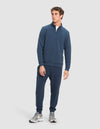 A man wears Cozy Earth's Men's StretchTech Quarter Zip and matching jogger pants with light gray sneakers, standing slightly turned with a neutral expression against a plain light background.|Color:Eclipse