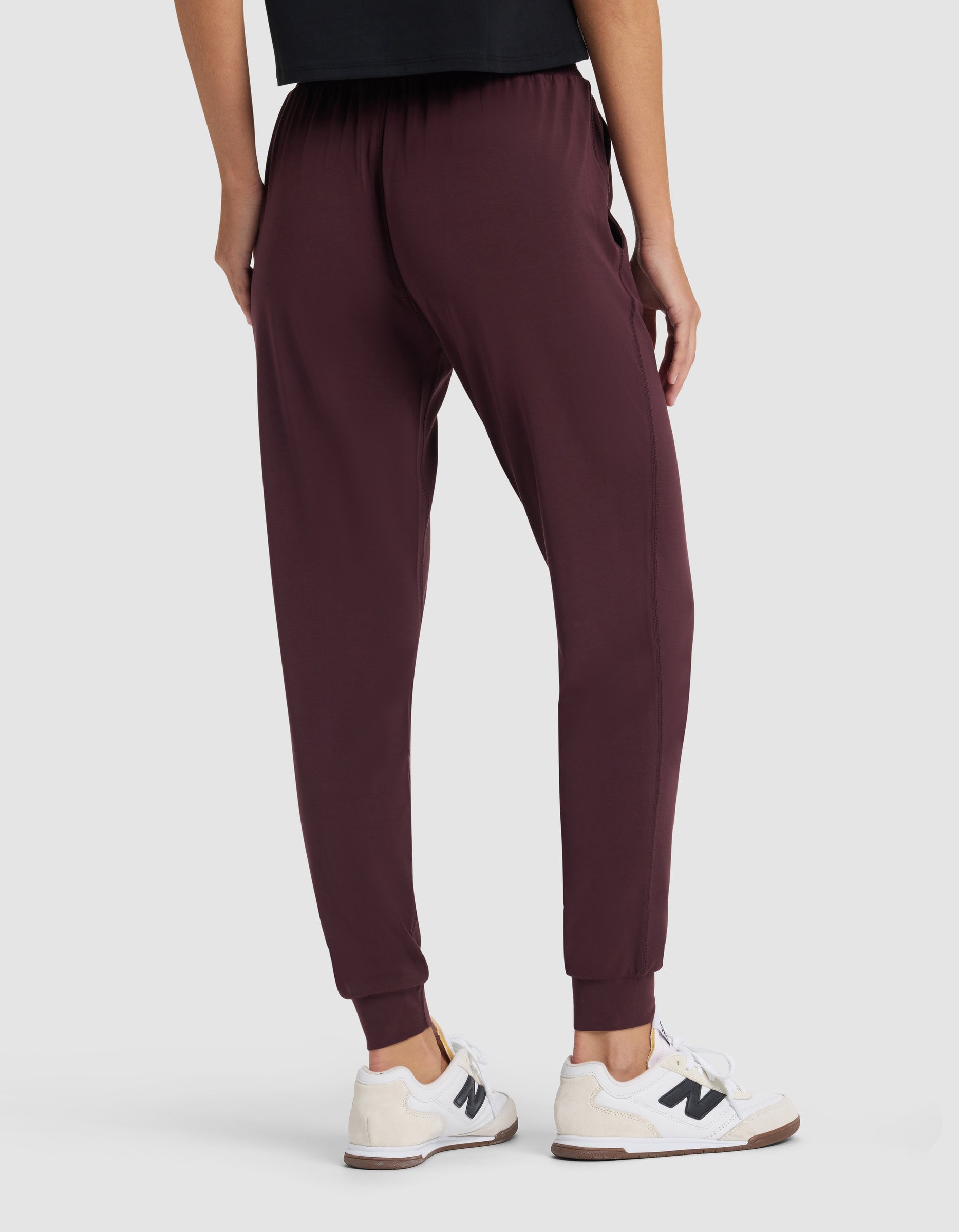 A person wearing Cozy Earth Women's Studio Jogger in burgundy and white sneakers, shown from the back with only their lower half visible against a plain light background.