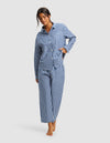 A woman stands barefoot against a plain light background, wearing the Cozy Earth Women's Sutton Long Sleeve Pajama Set, featuring a blue and white checkered button-up top and matching loose-fitting pants.|Color:Pacific Gingham