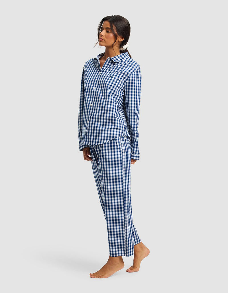 A woman stands barefoot against a light grey background, wearing the Cozy Earth Women's Sutton Long Sleeve Pajama Set in blue and white checkered print.