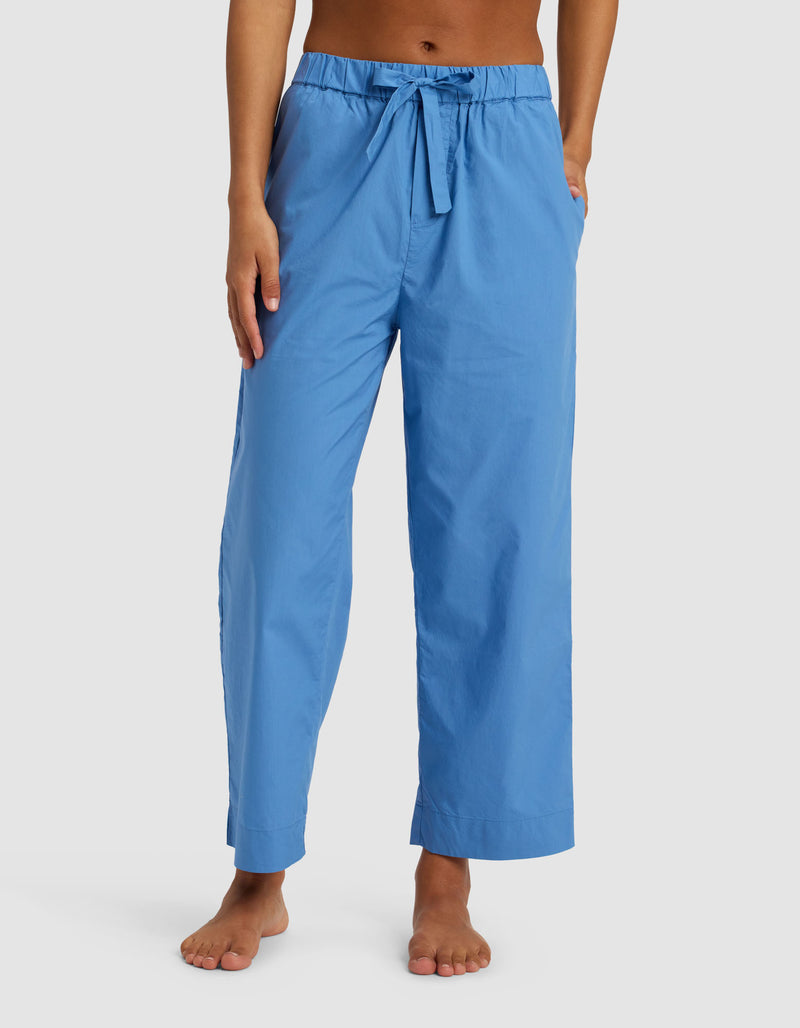 A woman wearing Cozy Earth's Women's Sutton Cropped Pajama Pant, featuring a drawstring waist and pockets in light blue, stands barefoot against a plain white background.