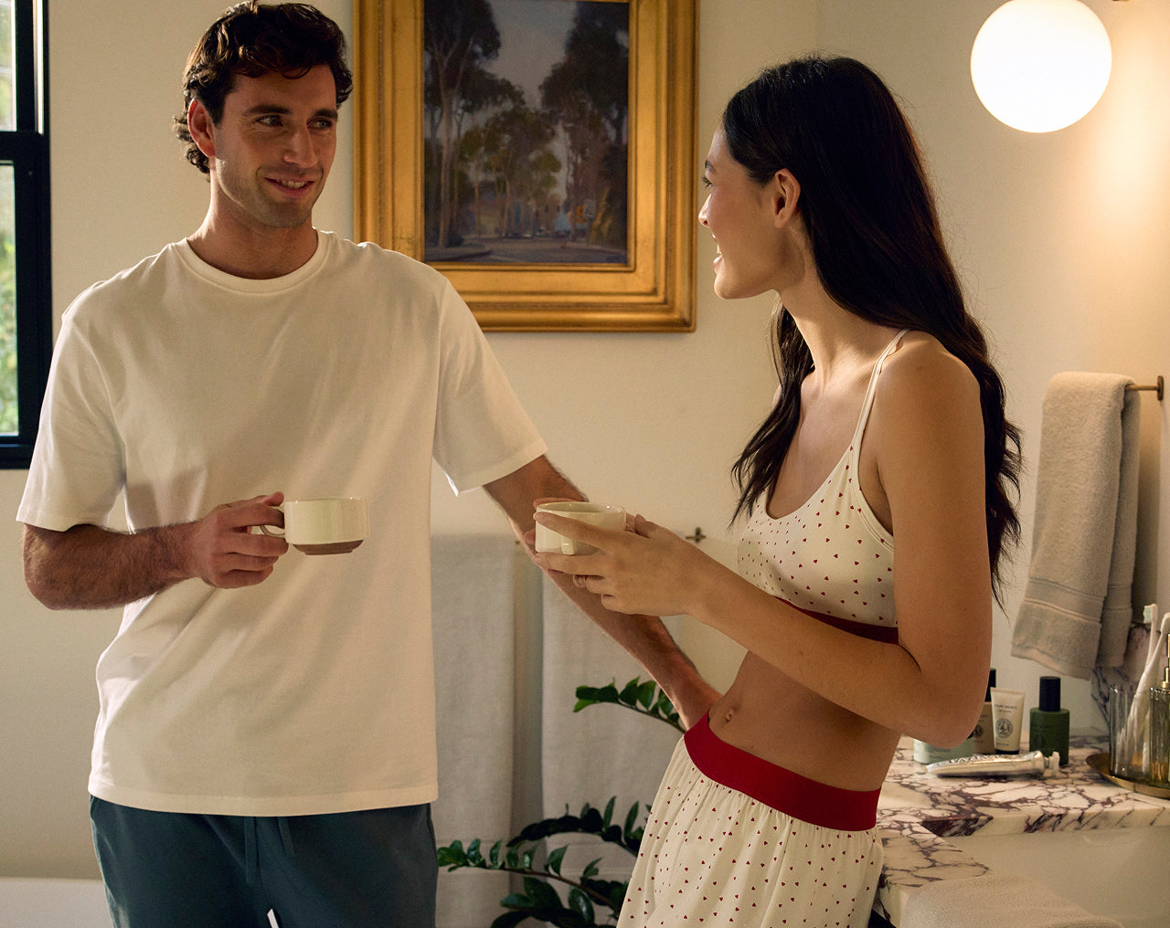 Man and woman in a bedroom setting holding cups.