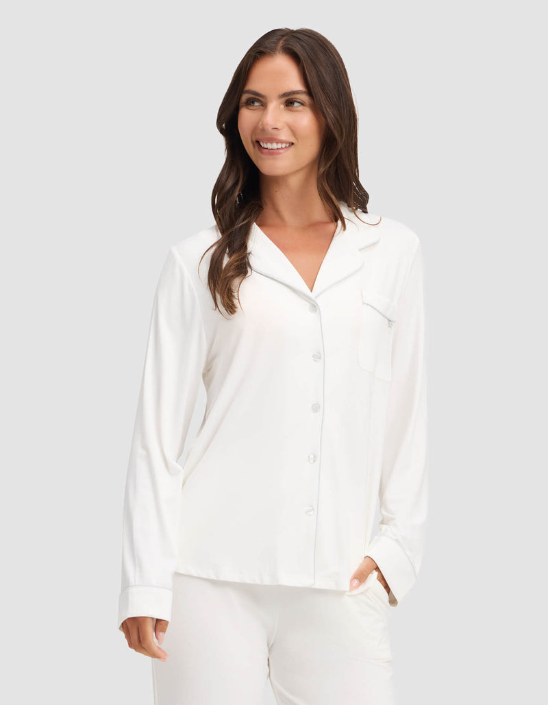 A woman wearing the Cozy Earth Women's Bamboo Stretch-Knit Long Sleeve Pajama Top is smiling while standing against a plain light gray background.