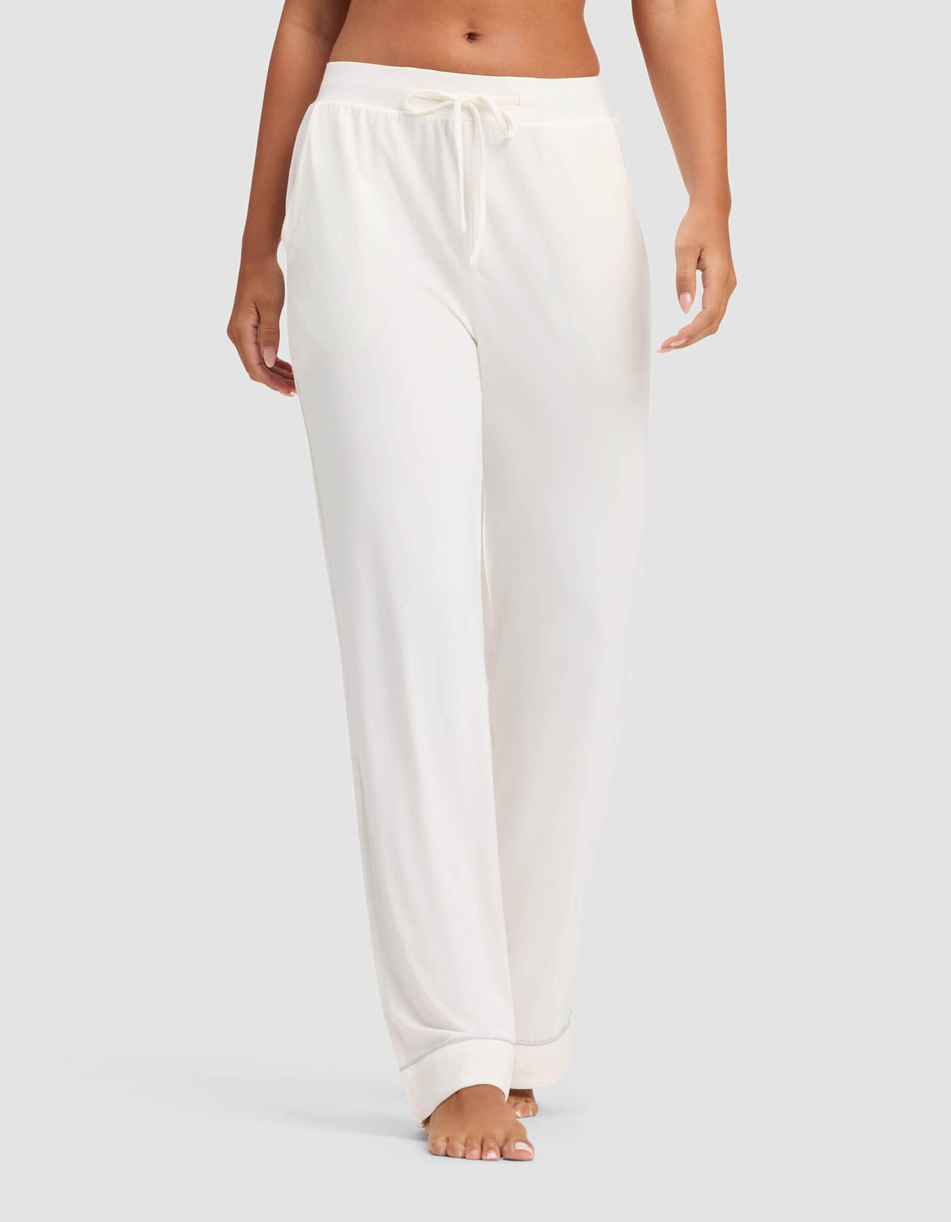 A woman models Cozy Earth's Women's Bamboo Stretch-Knit Pajama Pant, featuring a loose fit and drawstring waist, shown barefoot against a plain light background with only her lower torso and legs visible.|Color:Ivory
