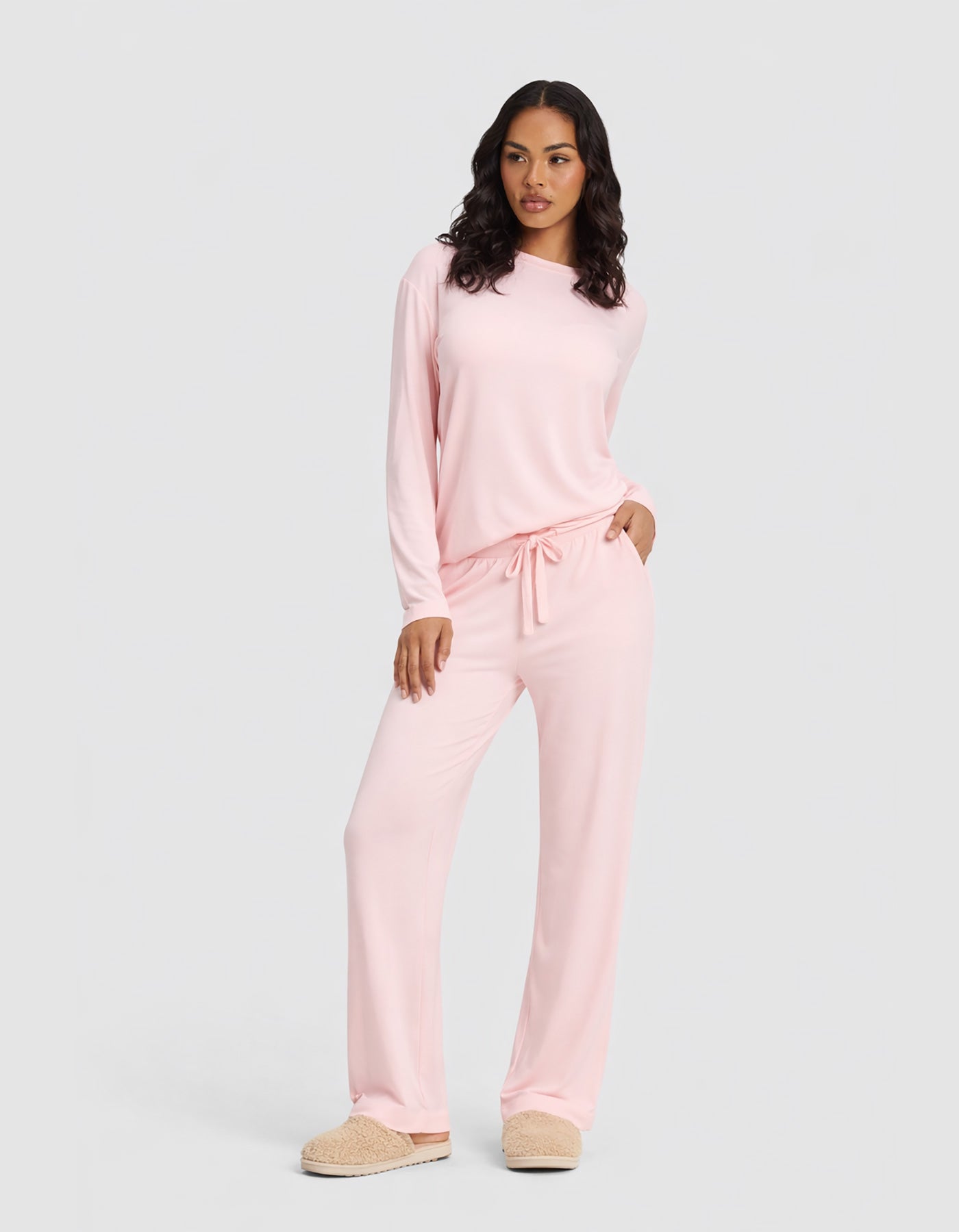 A woman wears the Cozy Earth Women's Bamboo Stretch-Knit Long Sleeve Lounge Tee & Pant Set in Blossom, paired with beige slippers, standing against a plain light gray background.