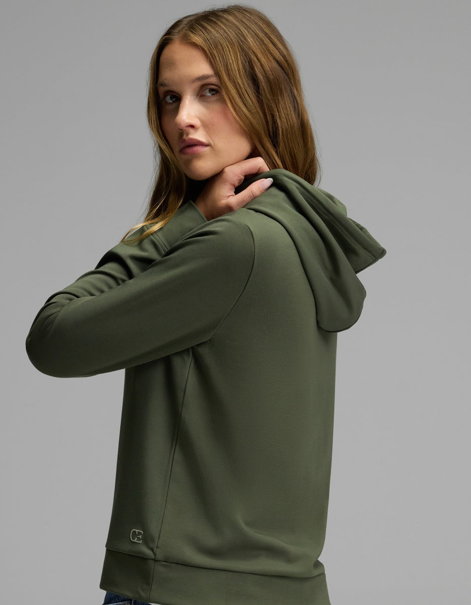 A woman models the Cozy Earth Women’s Brushed Bamboo Hoodie in olive green, glancing over her shoulder at the camera against a plain gray background.