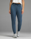 A person stands against a plain gray background wearing the Cozy Earth Women’s Brushed Bamboo Jogger in Dawn, paired with a white cropped shirt and gray athletic shoes.|Color:Dawn