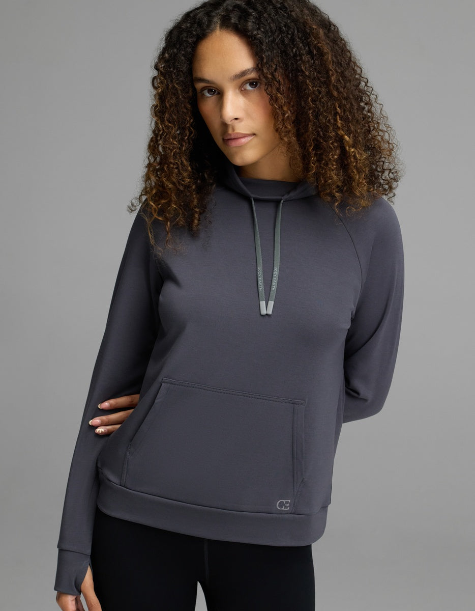 A woman with curly brown hair wears the Cozy Earth Women’s Brushed Bamboo Mock Neck in graphite, paired with black leggings, standing against a plain gray background.|Color:Graphite