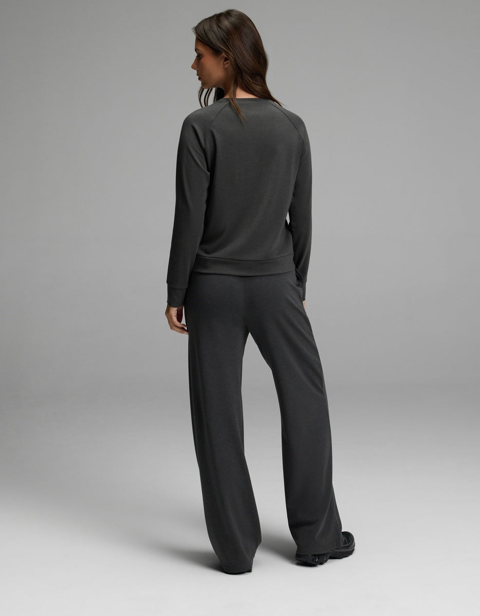 A woman with long brown hair stands facing away, wearing the Cozy Earth Women’s Brushed Bamboo Wide Leg Pull On Pant & Pullover Crew Set in dark gray against a plain light gray background.|Color:Charcoal
