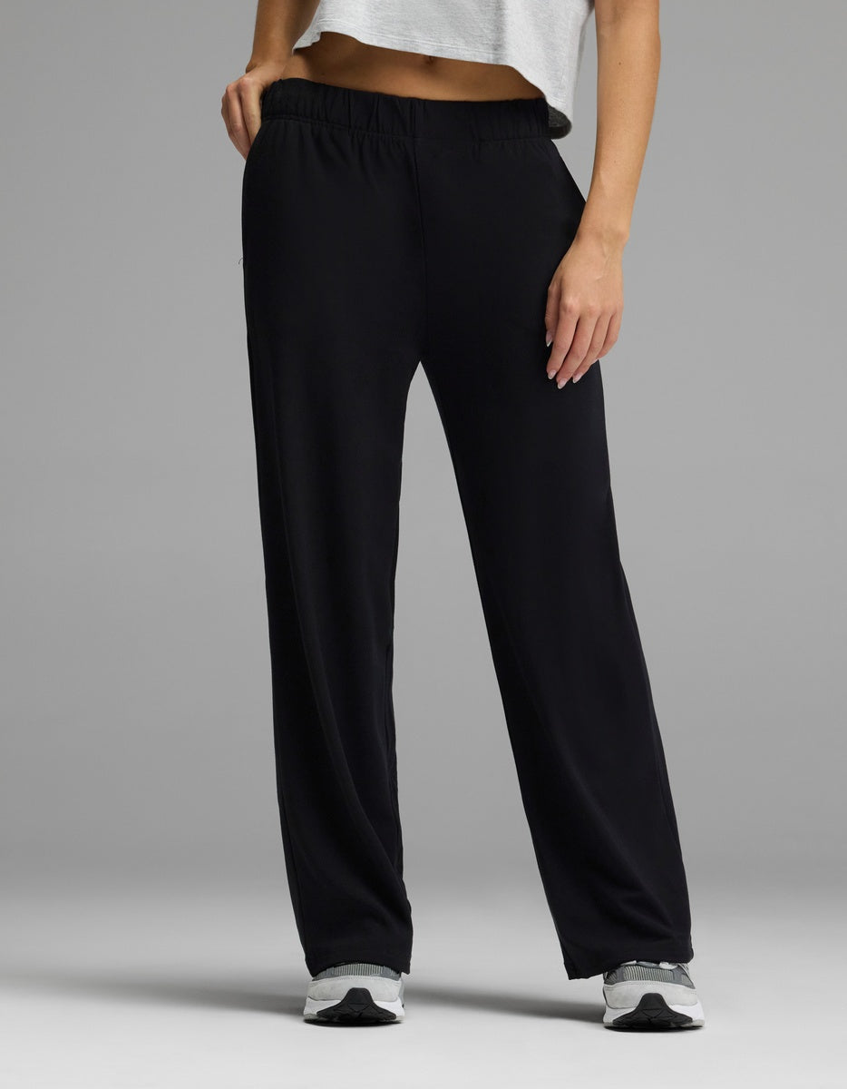 A person stands against a gray background—only the lower body is visible—wearing Cozy Earth’s Women’s Brushed Bamboo Wide Leg Pull-On Pant in black, paired with a white cropped top and white sneakers.