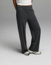 A woman wears Cozy Earth’s Women’s Brushed Bamboo Wide Leg Pull-On Pant in Charcoal, paired with white sneakers and a white top, standing with one leg crossed in front of the other against a plain gray background.|Color:Charcoal