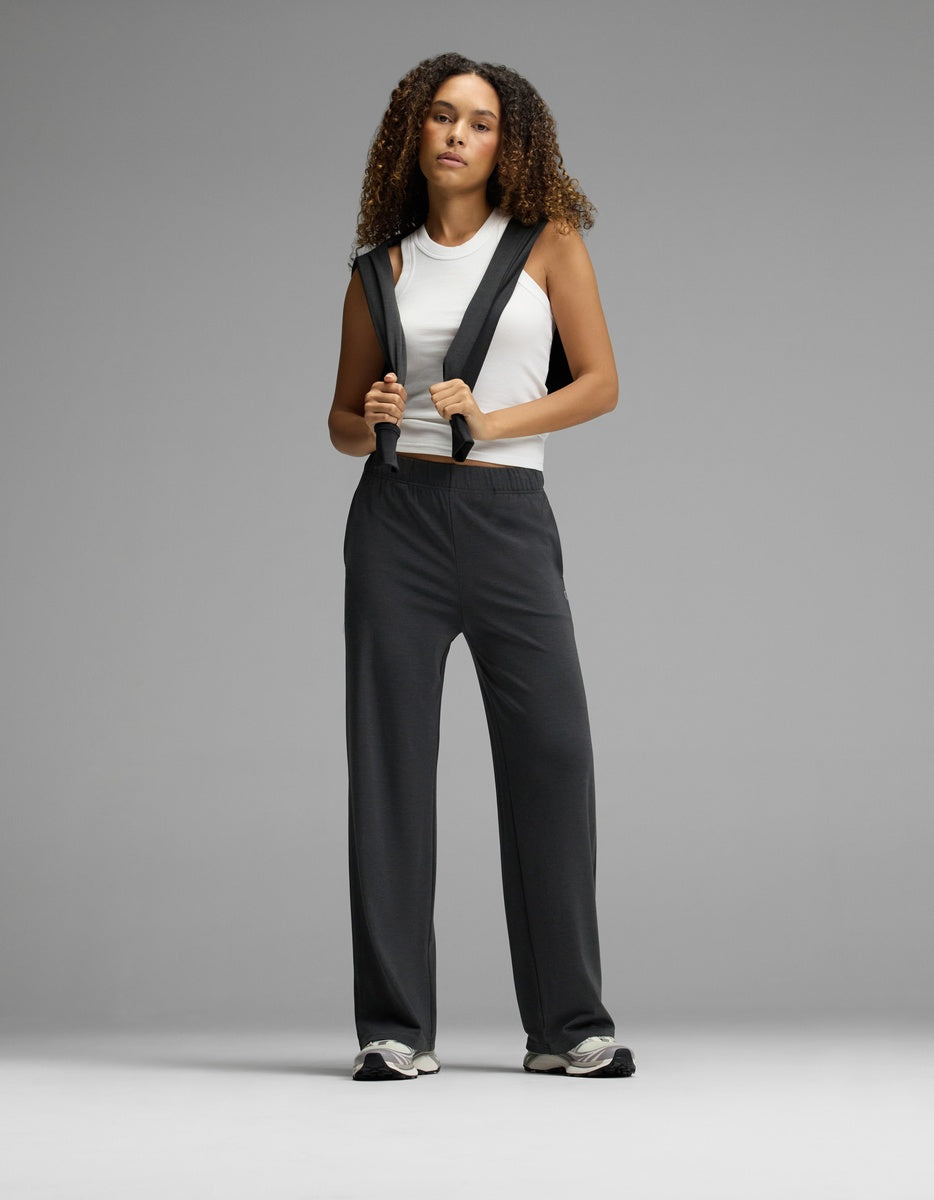 A person with curly hair wears a white sleeveless top and Cozy Earth’s Women’s Brushed Bamboo Wide Leg Pull-On Pant, standing confidently against a plain gray background.