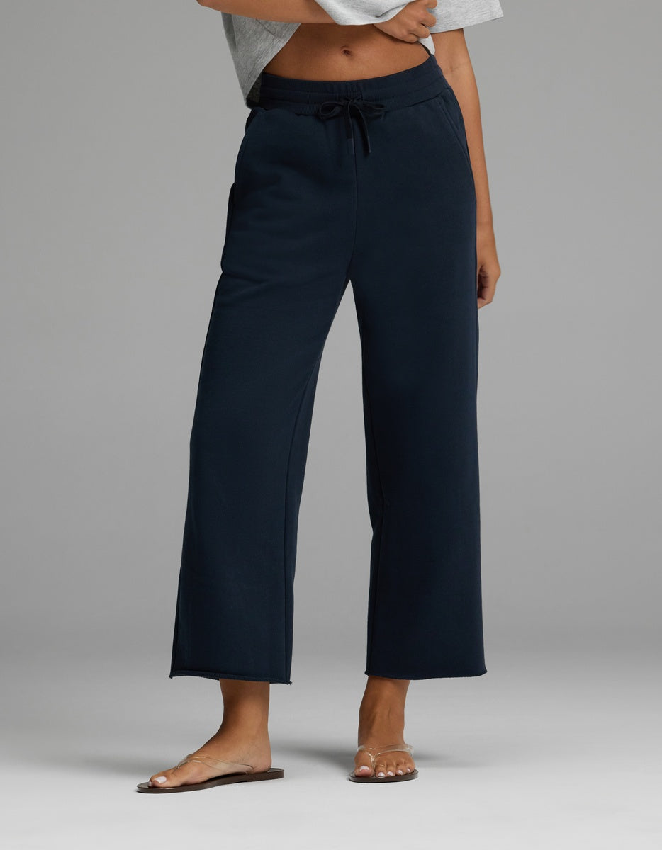 A person is wearing the Cozy Earth Women’s Chelsea Cropped Pant in Eclipse, featuring a drawstring waist and wide-leg silhouette, paired with a light gray cropped top and brown sandals. Only the lower torso and legs are visible, standing against a plain gray background.|Color:Eclipse