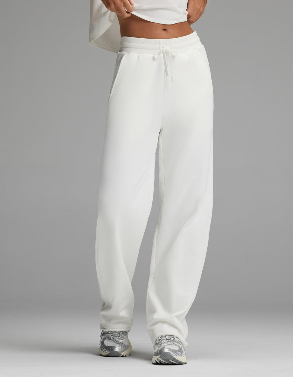A person stands against a plain gray background wearing the Cozy Earth Women’s Chelsea Pant in Bone and a white cropped top, paired with gray sneakers. Their face is not visible.|Color:Bone