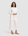 A smiling woman stands barefoot against a light gray background, wearing the Cozy Earth Women's Chelsea Set—loose-fitting, long-sleeved white top and matching wide-leg pants. |Color:Bone