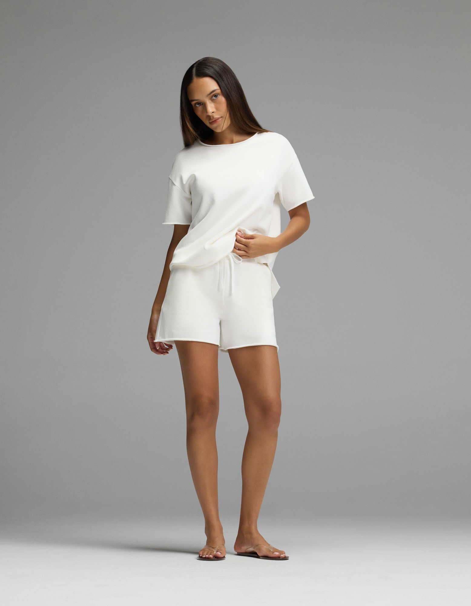 A woman stands barefoot against a gray background, wearing Cozy Earth’s Women’s Chelsea Short Sleeve Set in white, with her right hand resting in her pocket.|Color:Bone